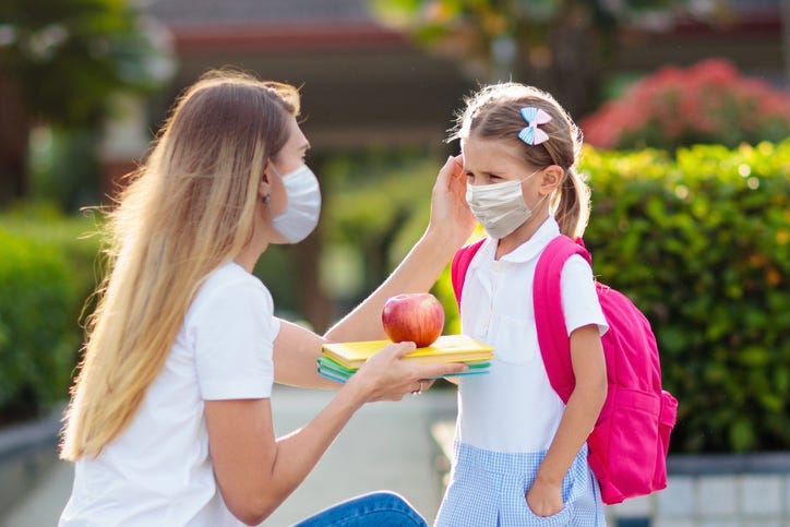 Woman drops off child at school while both wear masks