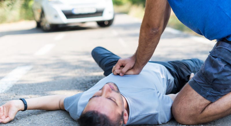 A man performs CPR on a another man laying on the ground