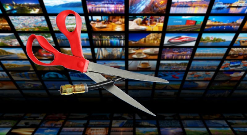 Image shows scissors cutting through a coaxial cable in front of a bank of tv screens