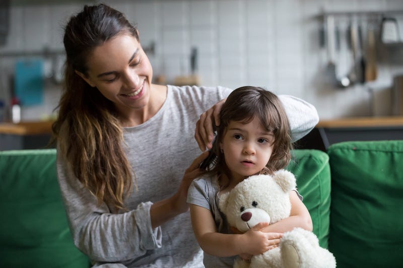 Caring loving mother brushing kid daughters hair sitting on sofa.