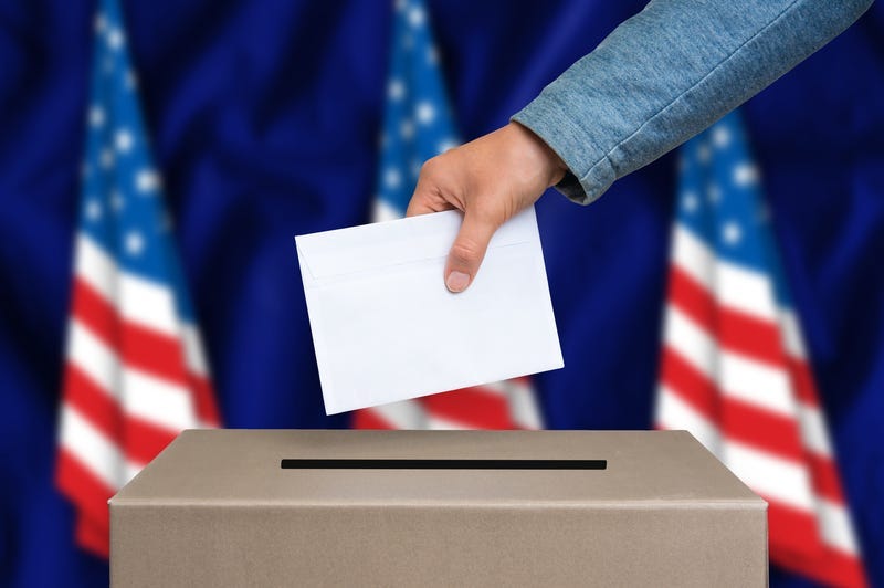 The hand of woman putting her vote in the ballot box. American flags on background.