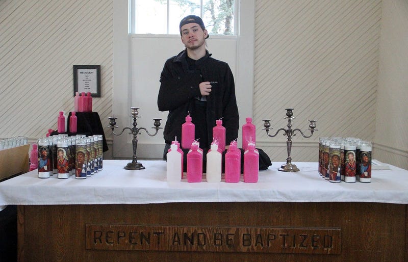 Artist FREEKYBEAR stands in front of candles inspired by trap culture at the TRAP CHAPEL pop-up art gallery in Atlanta
