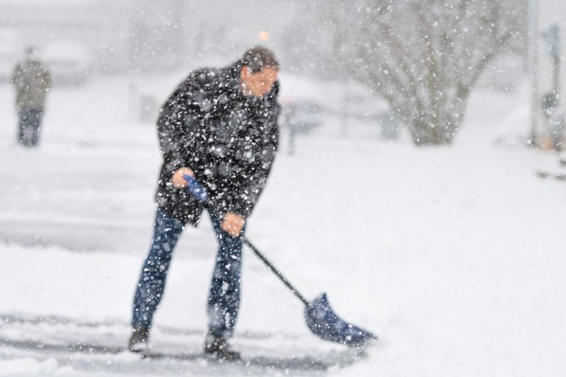 Man in winter coat shoveling driveway during heavy snowstorm.