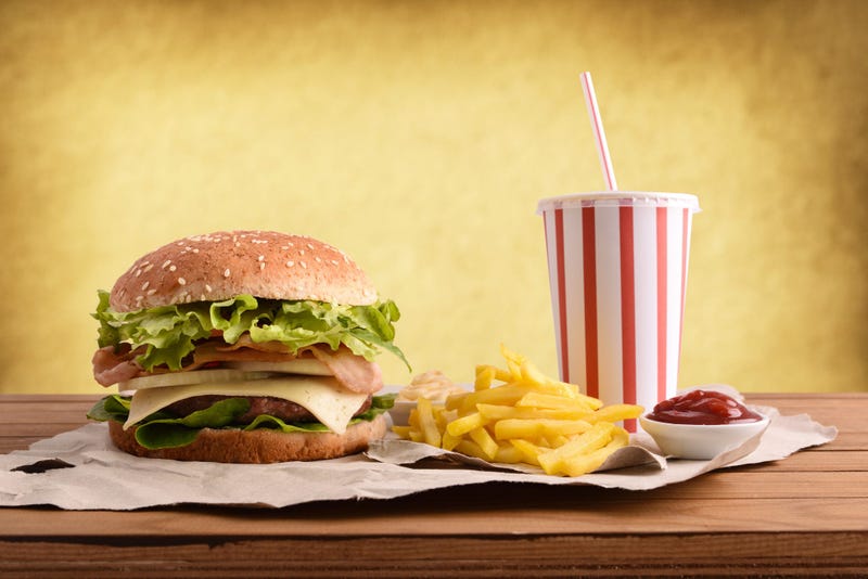 Beef burger with bacon and onion accompanied by chips, soda and souces on wooden table with golden backgorund.