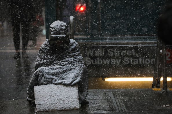 A homeless man sits in the falling snow in the Financial District, January 30, 2019 in New York City.
