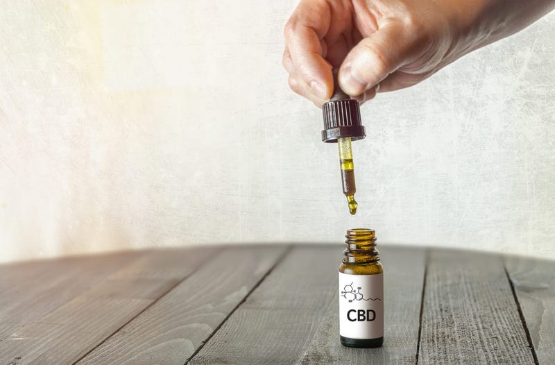 Hand holding pipette with CBD oil on wooden table