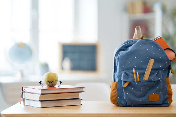 Apple, pile of books and backpack on the desk at the elementary school.