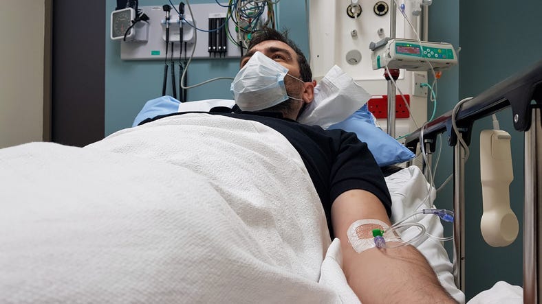 Young man lying in hospital bed. Recovering in modern hospital wards, covered with blanket, face mask and with intravenous needle in his arm
