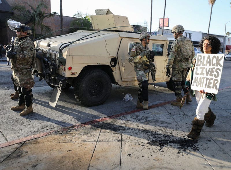 A woman carries a 'Black Lives Matter' sign past U.S. National Guard troops in the Fairfax District, an area damaged during yesterday's unrest, after the troops were activated by California Governor Gavin Newsom following violent demonstrations.