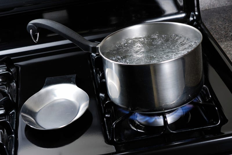 Pot of water boiling on a black natural gas stove.
