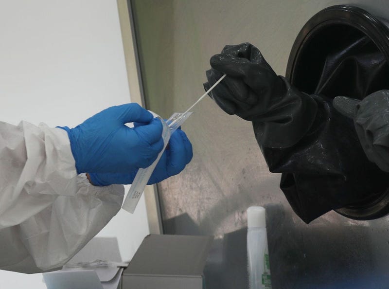 A nurse receives a swab to test a person through a glass pane in the Aardvark Mobile Health’s Mobile Covid-19 Testing Truck