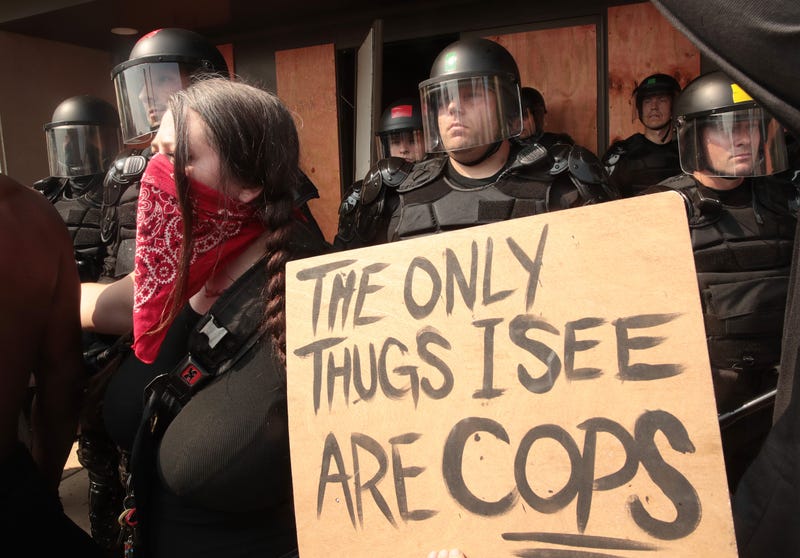 olice stand guard as woman protests with a sign written "the only thugs I see are cops" the day after a Black man was shot by police causing outrage and local unrest in the city on August 24, 2020 in Kenosha, Wisconsin.