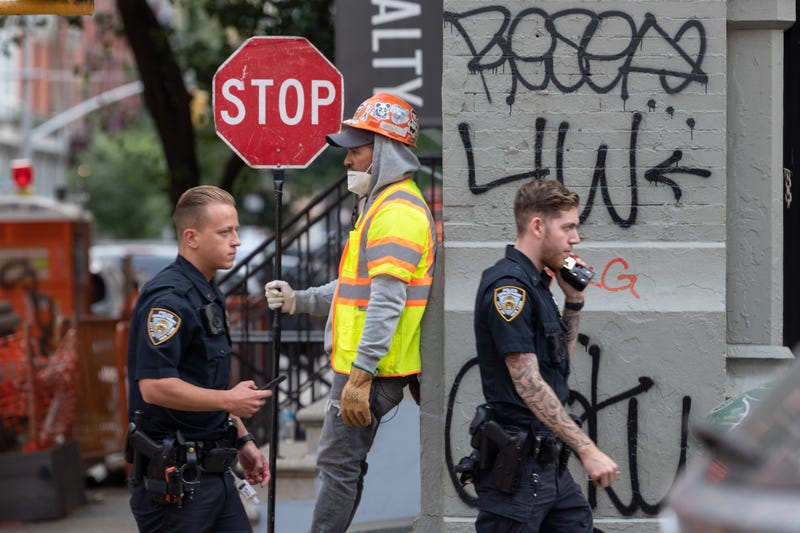 NYPD officers without masks walk past a construction worker holding a stop sign as the city continues Phase 4 of re-opening following restrictions imposed to slow the spread of coronavirus on September 16, 2020 in New York City.