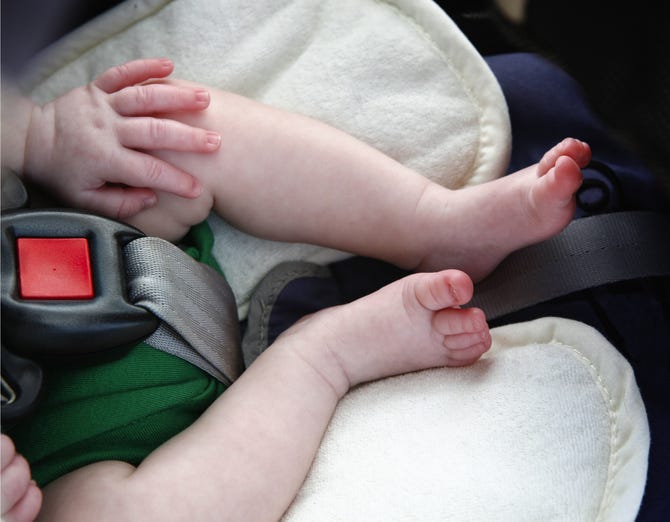 Legs and hand of little child in car seat.
