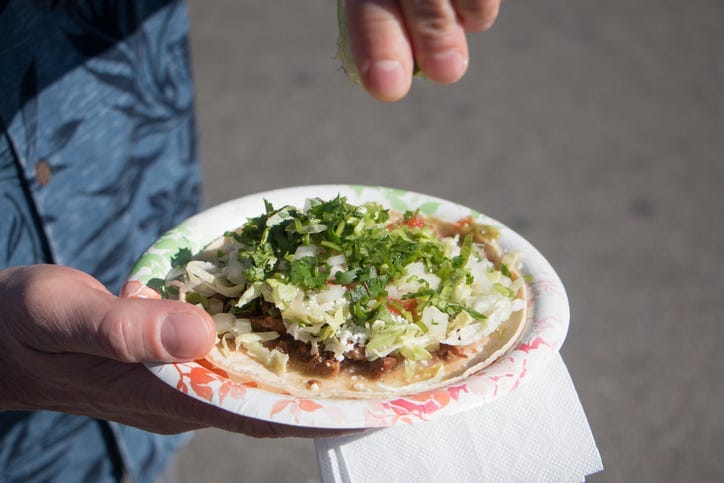 A lime is being squeezed onto a carne asada taco on a paper plate.