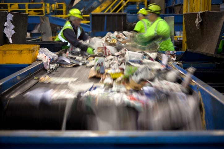 Workers separating paper and plastic on a conveyor belt in a recycling facility.