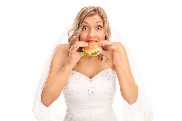 Surprised blond bride eating a sandwich and looking at the camera isolated on white background