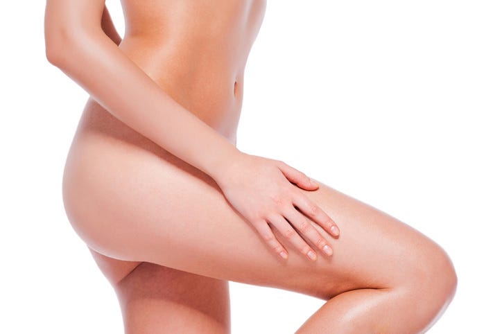 Close-up of young naked woman touching her leg while standing against white background