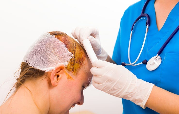 Surgeon with protective glove bandaging smiling victim's head after skull fraction.