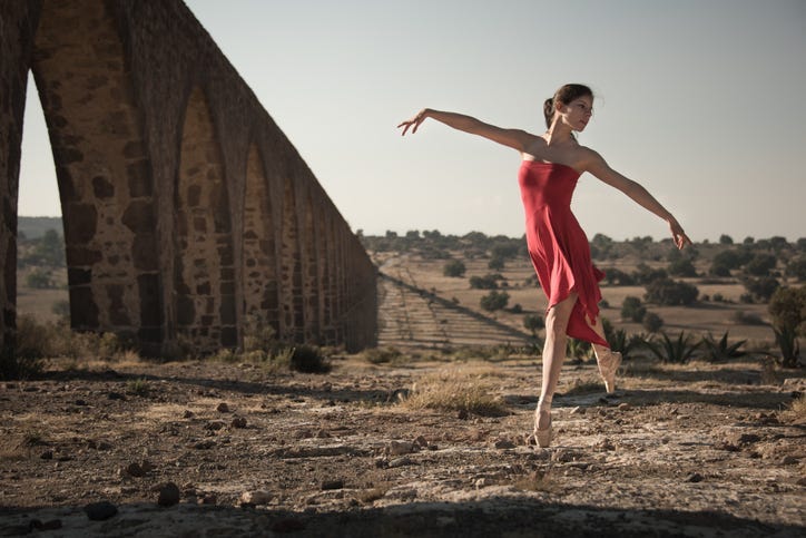 Ballerina wearing with a red dress and dancing in a colonial landscape.