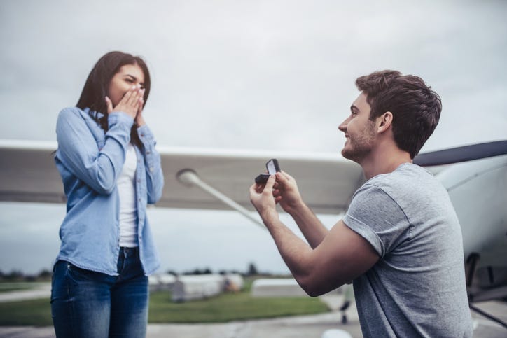 Beautiful romantic couple is standing near private plane in airport. Handsome man is making proposal to his attractive young woman.