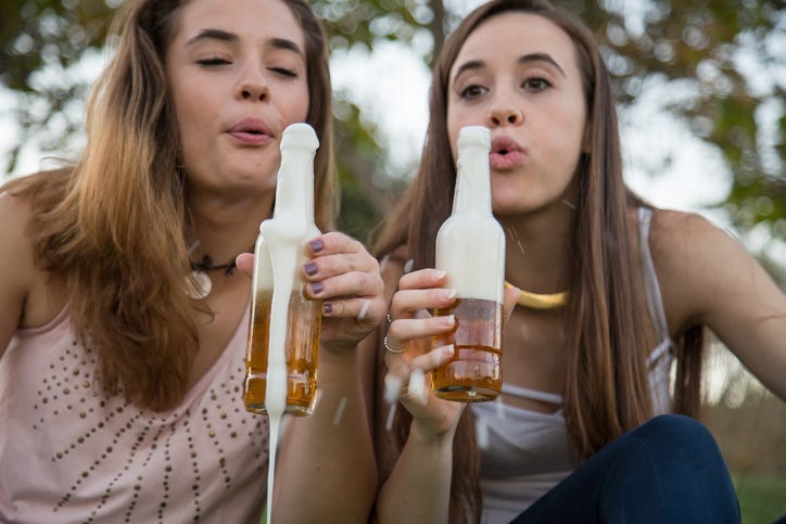 Two young laughing women celebrating with beer in park