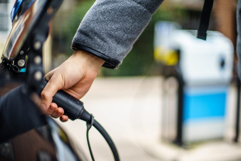 Close-up image of person's hand attaching charger cord to electric vehicle