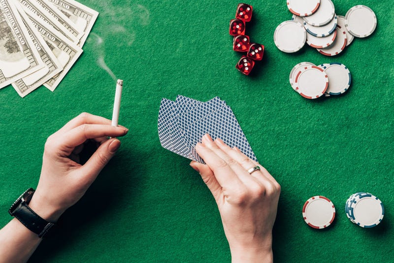 Woman holding cigarette and playing cards by casino table