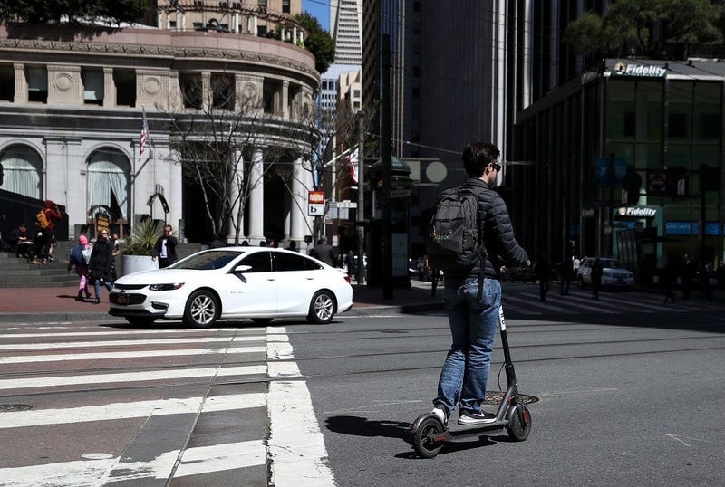 Guy rides motorized scooter through metro area.