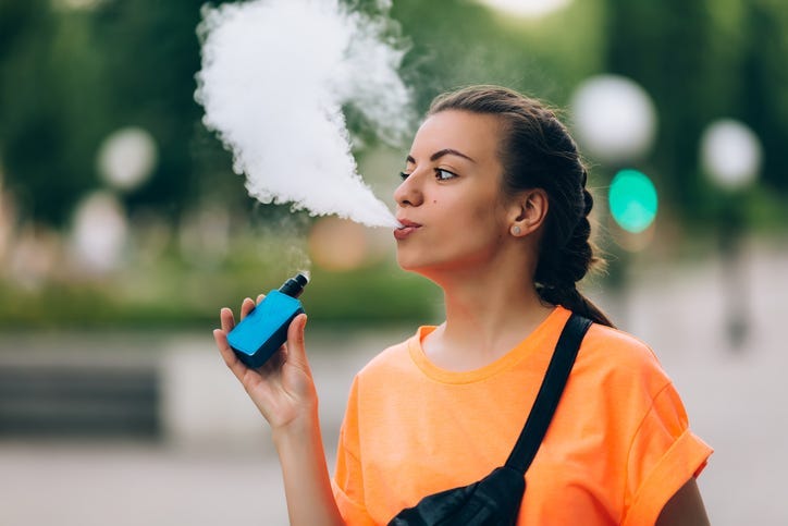 Pretty young girl vape popular ecig gadget,vaping device.Happy brunette vaper girl with e-cig.Portrait of smoker female model with electronic cigarette vaporizer.Ejuice vaping with fruit flavor liquid