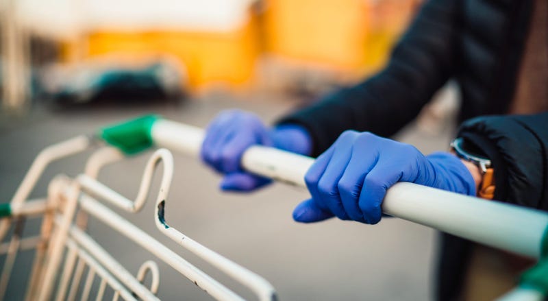 A woman wearing medical gloves grasps the handlebar of a shopping cart