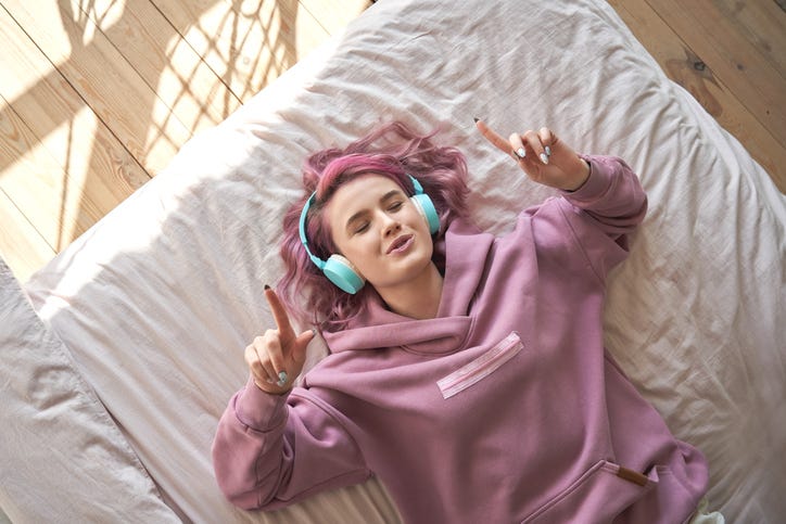 Girl listening to music on headphones on a bed