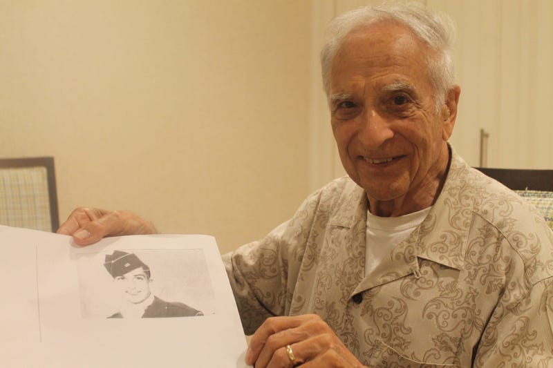 Frank Cohn holding a picture of himself in uniform during World War II.