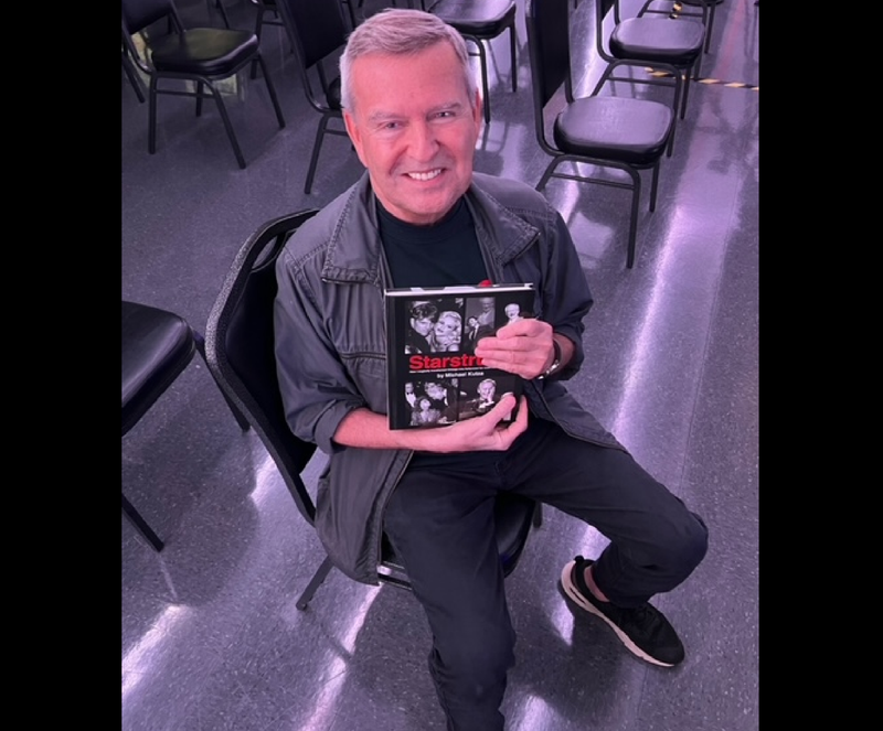 Michael Kutza sits on a chair holding his latest book