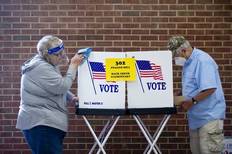 Glenda Patsel, left, wipes down a voting booth as Bobby J. Lambert fills out his ballot for the senate Republican candidates primary election, Tuesday, June 23, 2020, at Hidden Valley Middle School in Roanoke, Va.