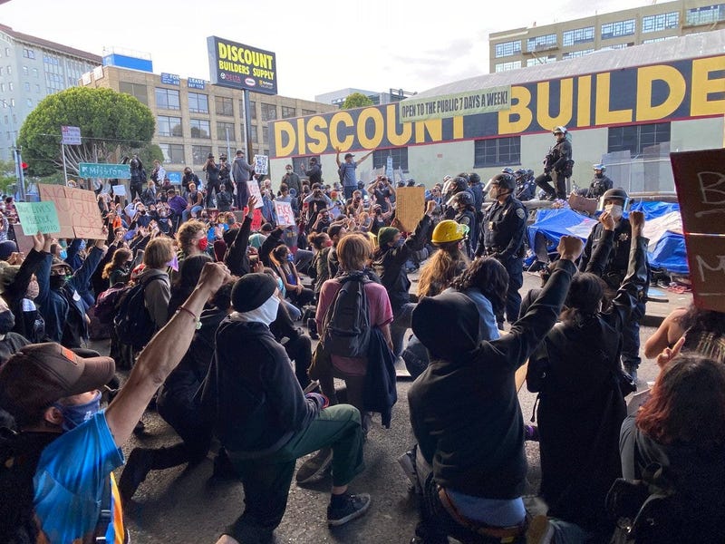Protestors blocking 13th St. under the freeway in San Francisco kneeling in front of police.