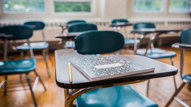 An empty school classroom with a notebook and pencil on desk