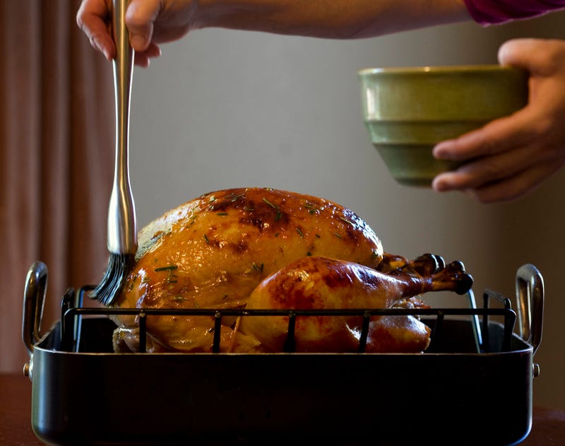 An unseen cook brushes a roast turkey with oil
