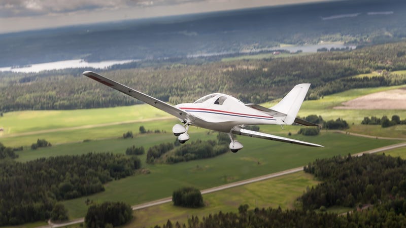 An ultralight flying above a flat landscape with forests, fields and river. The sky is cloudy, like before a thunderstorm