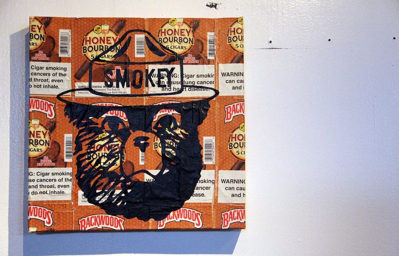 A painting of Smokey the Bear over plastered Backwoods wrappers at the TRAP CHAPEL pop-up art gallery in Atlanta