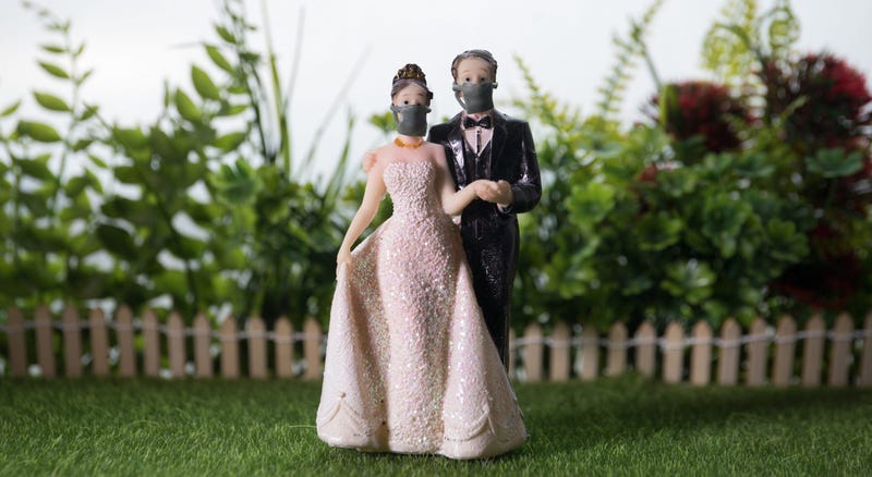 A wedding cake topper of bride and groom wearing face masks