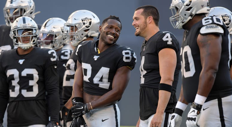 Oakland Raiders wide receiver Antonio Brown (84) and quarterback Derek Carr (4) hold their helmets before a game against the Green Bay Packers at Investors Group Field Oakland Raiders wide receiver Antonio Brown (84) and quarterback Derek Carr (4) hold their helmets before a game against the Green Bay Packers at Investors Group Field