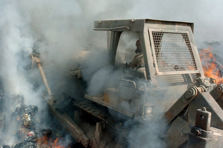 Smoke billows in from all sides as Sgt. Richard Ganske, 84th Combat Engineer Battalion, pushes a bulldozer deep into the flames of a burn pit in Balad, Iraq to keep burnable items constantly ablaze, disposing of them so they do not clutter up the post. BurnPits3