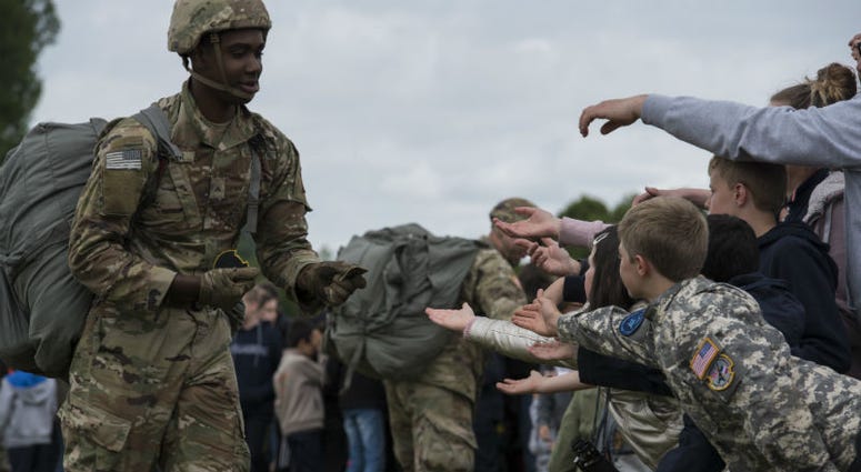 U.S. static-line paratrooper gives his military service patches to the eager hands of French boys and girls. Over 1,000 U.S. paratroopers participate in largest airborne operation since WWII to commemorate 75th anniversary of D-Day.