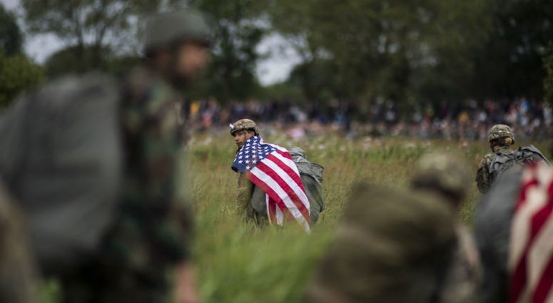 A U.S. paratrooper walks with a U.S. flag on his shoulders after conducting a static-line jump. Over 1,000 U.S. paratroopers participate in largest airborne operation since WWII to commemorate 75th anniversary of D-Day.
