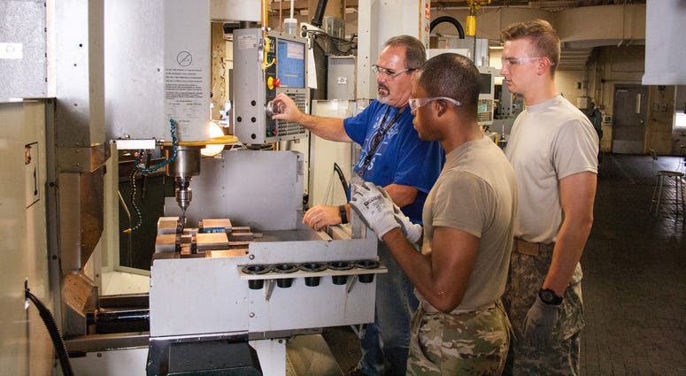 Cadets Shamus Shields (center) and Jermell Chester (near), watch as a machine is operated to measure levelness of a vice in preparation to make a hammer during their internship with RIA-JMTC, Rock Island Arsenal, Illinois, July 26, 2017.