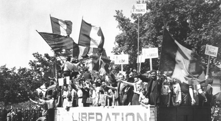 In this Aug. 28, 1944 file photo, a truck load of Parisians waving flags and carrying Vive De Gaulle banners drives through the streets