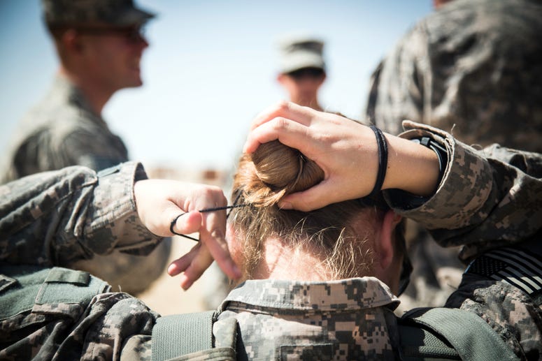 Spc. Nina Bray, intelligence analyst, Headquarters and Headquarters Company, 204th Brigade Support Battalion, 2nd Armored Brigade Combat Team, 4th Infantry Division, fixes her hair bun before putting on her body armor at a M203/M320 40 mm grenade launcher