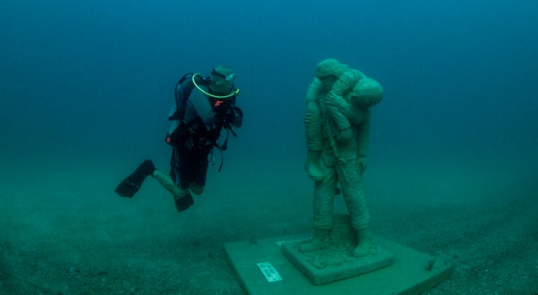 A diver comes face-to-face with one of 12 life-size statues of members of the Armed Forces that make up the Circle of Heroes underwater veterans memorial. DiverStatue