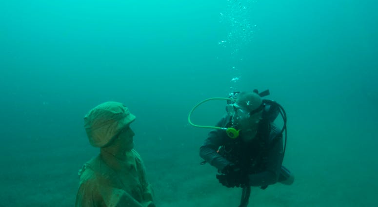 A diver comes face-to-face with one of 12 life-size statues of members of the Armed Forces that make up the Circle of Heroes underwater veterans memorial. DiverStatue